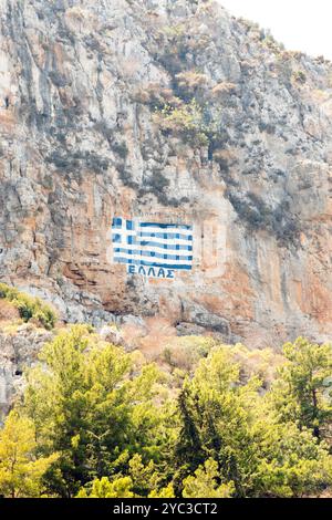 Una bandiera greca dipinta su una scogliera con le parole Grecia scritte in alfabeto greco, sopra l'isola greca di Kastellorizo o Meis in Grecia, Europa Foto Stock