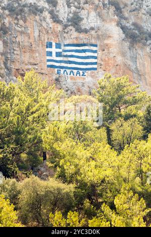 Una bandiera greca dipinta su una scogliera con le parole Grecia scritte in alfabeto greco, sopra l'isola greca di Kastellorizo o Meis in Grecia, Europa Foto Stock