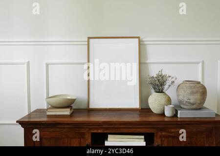 Elegante disposizione delle credenze. Armadietto per credenze in mogano. Cornice verticale vuota per poster in legno. Vasi di argilla, fiori secchi, libri, candele. Foto Stock