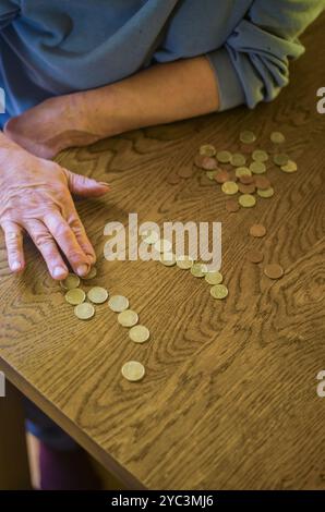 donna anziana seduta miseramente a tavola a casa e a contare le monete. Foto di alta qualità Foto Stock