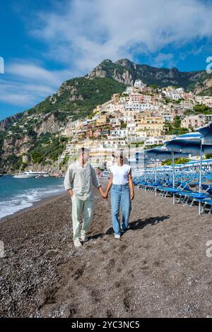 Un paio cammina mano nella mano lungo la costa di ciottoli di Positano, con le case colorate sulla scogliera dietro di loro. Positano sulla Costiera Amalfitana Foto Stock