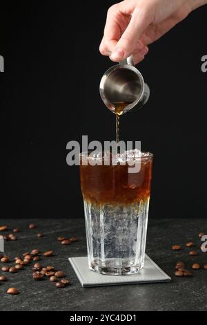 Donna che prepara rinfrescanti bevande toniche per espresso al tavolo buio, primo piano Foto Stock