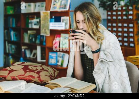 Romny, Ucraina, 29 settembre 2019: Una giovane donna attraente è seduta a un tavolo in una vecchia biblioteca atmosferica con una tazza di tè in mano e re Foto Stock