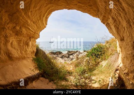 Antico bacino di carenaggio scolpito in arenaria sulla spiaggia di sa Cala e nave a vela sullo sfondo (la Mola, Formentera, Isole Baleari, Mar Mediterraneo, Spagna) Foto Stock