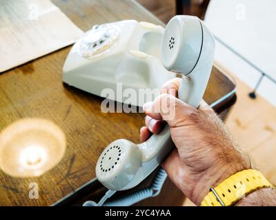 Una persona che tiene il ricevitore di un telefono rotativo vintage su una scrivania di legno, evocando nostalgia e temi di comunicazione retrò Foto Stock