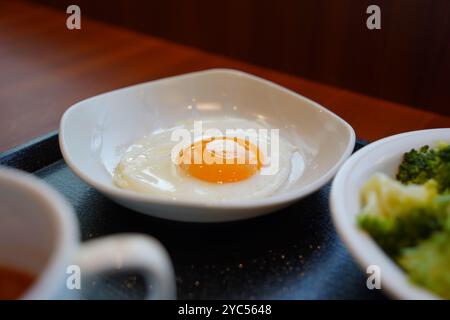 Uovo fritto in un recipiente bianco su un tavolo di legno Foto Stock