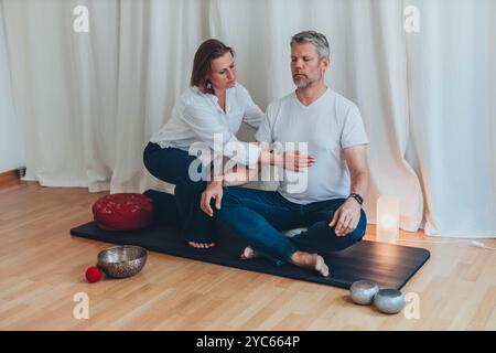 Uomo e donna che praticano la respirazione consapevole insieme durante una sessione di meditazione, seduti su tappeti con ciotole sonore. Foto di alta qualità Foto Stock