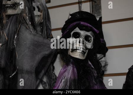 Scheletro spaventoso o teschio umano con cappello a velo nero e nastro viola esposto in negozio Foto Stock