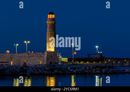 Il faro illuminato di Rethymno al crepuscolo, che si erge alto lungo il porto di Creta, in Grecia. Il caldo bagliore del faro contrasta splendidamente con il wi-fi Foto Stock