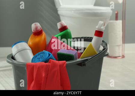 Secchio con diversi detergenti per WC, spugna, sacchetti per la spazzatura, stracci e guanti in bagno, primo piano Foto Stock