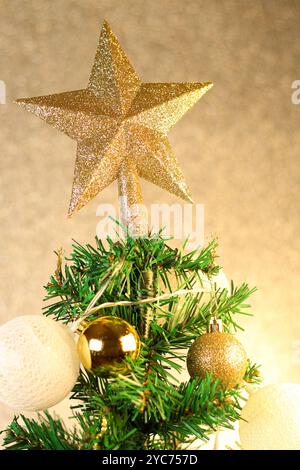Foto ravvicinata di un albero di Natale con una stella in cima, decorata con sfere e luci gialle. Preparazione per l'idea di festeggiare il nuovo anno. Foto Stock