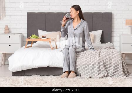 Giovane donna asiatica che beve vino a letto in camera da letto Foto Stock