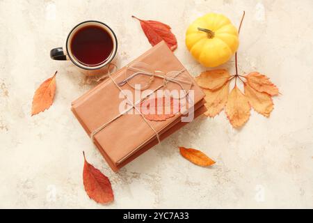 Composizione con pila di libri, tazza di tè e foglie autunnali su sfondo grunge chiaro Foto Stock