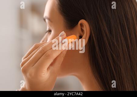 Giovane donna che mette il tappo dell'orecchio in camera da letto, primo piano Foto Stock