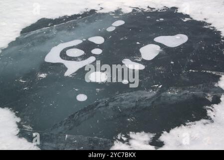Superficie crepe del lago ghiacciato di Baikal con bolle di metano gelate e montagna sullo sfondo nella stagione invernale sull'isola di South Olkhon. Foto Stock