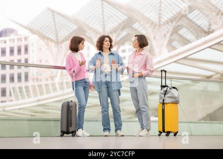 Tre amici chiacchierano in un moderno centro di trasporto con i bagagli in una giornata di sole Foto Stock