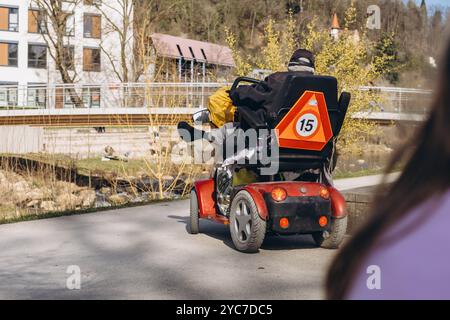 Persona in uno scooter specializzato per disabili, che guida attraverso un parco. Foto di alta qualità Foto Stock