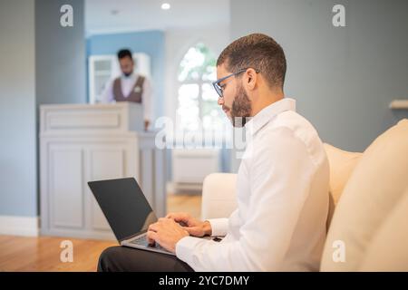 Un uomo lavora con il suo computer portatile nella hall di un hotel Foto Stock