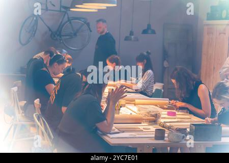 Cracovia, Polonia - 21 ottobre 2024: Un gruppo di persone focalizzate si è impegnato in un laboratorio di ceramica creativa, realizzando con cura pezzi di ceramica su un lungo tratto Foto Stock