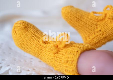 Un paio di allegri stivaletti gialli lavorati a mano si adattano perfettamente ai piedi dei bambini, sfoggiando un design accogliente con un fiocco carino. Lo sfondo presenta un bianco morbido Foto Stock