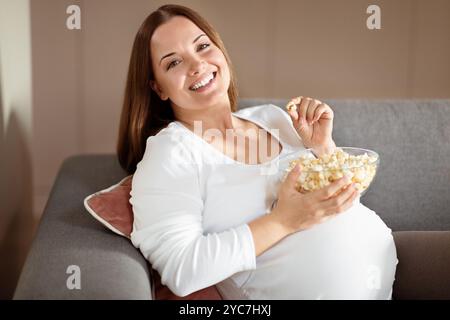 Donna incinta che si diverte mentre si rilassa sul divano a casa Foto Stock