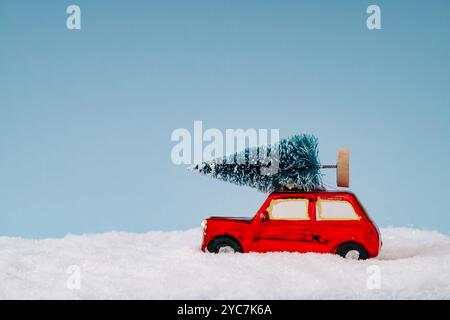 Composizione invernale realizzata con auto rossa con albero di Natale e neve su sfondo blu. Concetto minimale di Natale e Capodanno. Feste creative Foto Stock