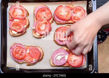 La mano di una donna mette una fetta di pomodoro su un panino prima di cuocere. Cucina casalinga. Foto Stock