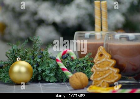 Una fotografia di Natale orizzontale che mostra due bicchieri di vetro trasparente riempiti di cioccolata calda. Bastoncini per waffle, bastoncini di caramelle, rami di pino, noci e anice Foto Stock
