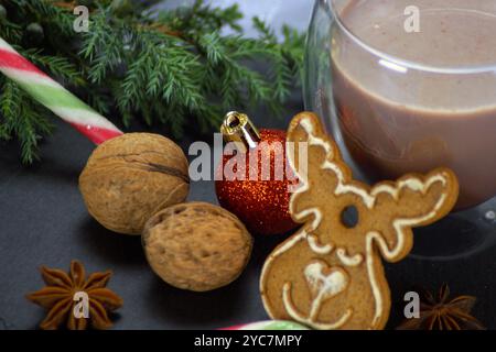 Due bicchieri di vetro trasparenti ripieni di cioccolata calda, un biscotto di pan di zenzero a forma di albero di Natale, un ramo di abete, noci e una canna da zucchero completano il Foto Stock