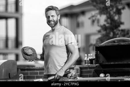 Uomo che si diverte a fare barbecue. Preparazione alla griglia con guru affumicato. uomo che grigia le sue carni preferite. cuoco che mostra le sue tecniche di barbecue durante l'evento di cucina Foto Stock