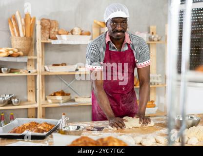 il fornaio maschile si trova al banco di lavoro, impastando e modellando l'impasto per preparare pane, croissant e baguette Foto Stock