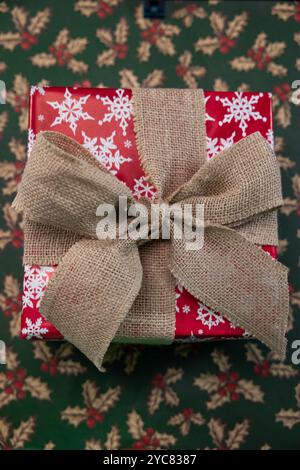 Regalo di Natale avvolto in carta Red Snowflake con arco Burlap su un tavolo Foto Stock