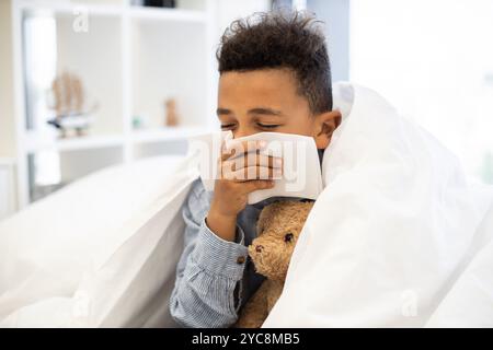 Il ragazzo soffia il naso sotto la coperta mentre tiene in mano l'orsacchiotto Foto Stock