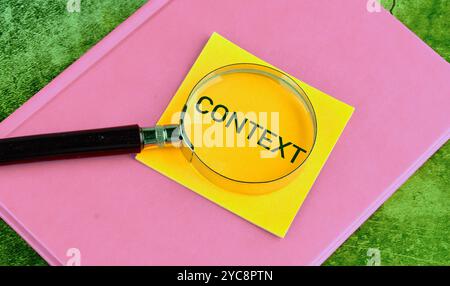 Simbolo del contesto concettuale. Copia spazio. Parola contestuale scritta su un adesivo giallo attraverso una lente d'ingrandimento posizionata su un taccuino rosa. Foto Stock