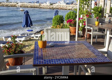 Fantastica mattinata sulla spiaggia di Santorini (o Creta o Spetses o Rodi o Mykonos) e porto in lontananza! Vista dalla maestosa caffetteria sulla spiaggia con un fantastico flowe Foto Stock