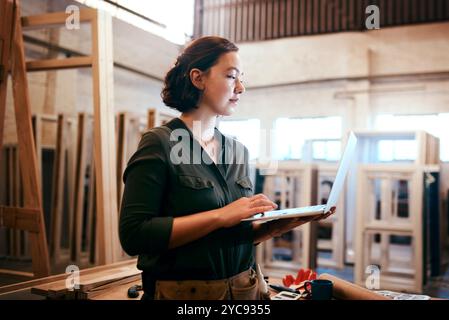 Industria, laptop e tipizzazione con una donna di falegname in officina per la lavorazione artigianale, la falegnameria o la lavorazione del legno. Computer, inventario e ordini online con Foto Stock