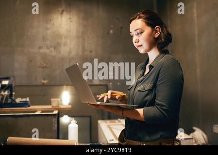 Laptop, falegname e tipizzazione con donna in officina per designer di mobili, fornitori di edifici e progetti. Lavorazione del legno, software CAD e pianificazione con Foto Stock