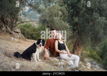 Una coppia si siede su una collina, godendosi un momento di pace con il loro Border Collie al loro fianco. Foto Stock