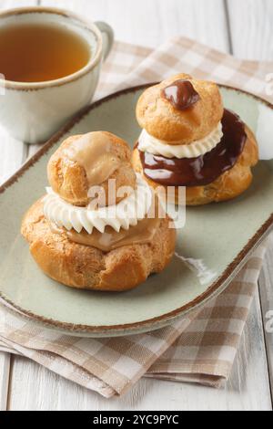 La pasticceria Religieuse è composta da due choux panini ripieni di crema pasticcera, ricoperti di ganache al cioccolato e decorati con il primo piano della crema sul piatto Foto Stock