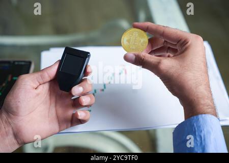 giovane trader indiano di criptovalute che tiene in mano bitcoin e portafoglio hardware. Concetto di sicurezza e criptovaluta. Foto Stock