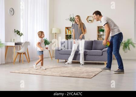 Famiglia felice che gioca con la palla a casa, genitori allegri e figlia che si divertono e si divertono. Foto Stock