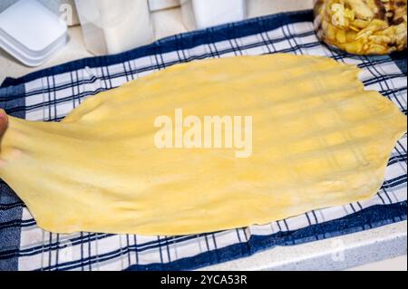 Estrazione dell'impasto fatto in casa per lo strudel su un asciugamano a scacchi, primo piano. Foto Stock