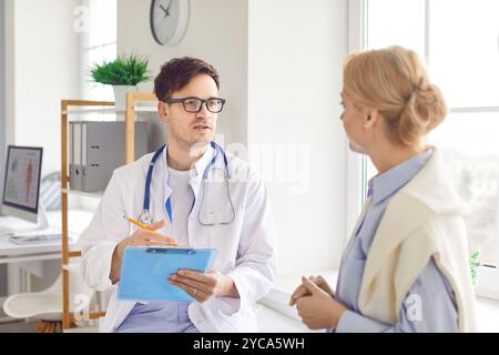 Giovane medico maschile che indossa uniforme medica bianca consulenza paziente femminile, parlando su consultazione Foto Stock