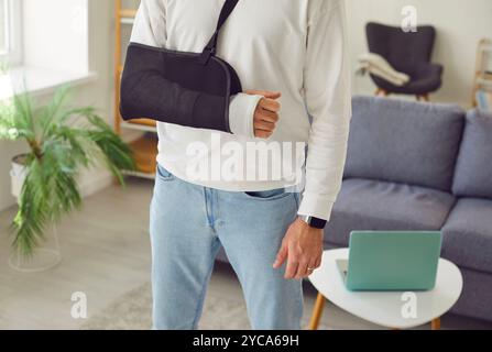 Uomo in piedi a casa in riabilitazione con il braccio rotto in gesso dopo una ferita. Foto Stock