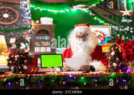 Babbo Natale controlla la sua lista cattiva o carina accanto al mockup isolato, preparandosi per il suo viaggio intorno al mondo per portare regali alla vigilia di Natale. Vecchio che rende felici i bambini con x mas. Foto Stock