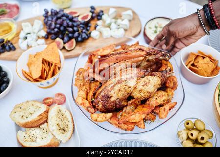 Primo piano di un irriconoscibile uomo afroamericano che mette sul tavolo da pranzo un delizioso piatto di pollo arrosto con patate dorate Foto Stock