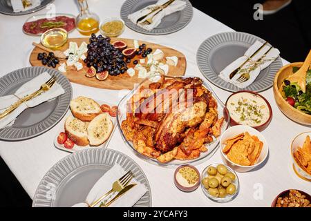 Ad angolo con pollo arrosto dorato sul tavolo da pranzo, servito con spuntini e piatti per feste all'aperto con flash Foto Stock