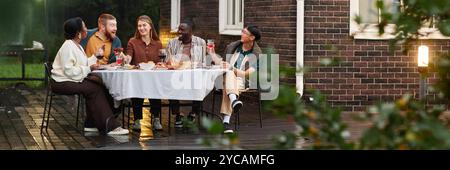 Riprese grandangolari di gruppi diversi di adulti che si godono una cena insieme nel patio all'aperto accanto allo spazio fotocopie della casa in mattoni Foto Stock