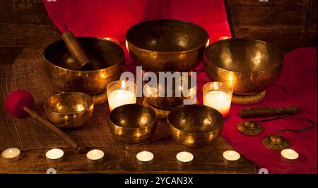 Set di ciotole e campane tibetane con candele accese su sfondo rosso Foto Stock