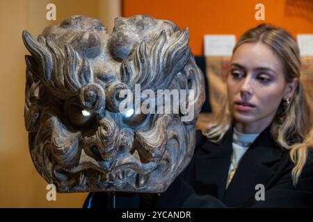 Londra, Regno Unito. 22 ottobre 2024. Un membro del personale con 'una maschera di legno dorato sovradimensionata', del XVII-XVIII secolo, in Giappone, sullo stand Patrick & Ondine Mestdagh ad un'anteprima della fiera LAPADA dell'Associazione dei concessionari di Arte e antiquariato. I rivenditori specializzati stanno presentando una vasta gamma di opere d'arte, design e antiquariato con la garanzia di autenticità grazie a un comitato di esperti composto da 70 membri che controlla in anticipo tutto ciò che è in vendita. La fiera si svolge dal 22 al 27 ottobre a Berkeley Square. Crediti: Stephen Chung / Alamy Live News Foto Stock